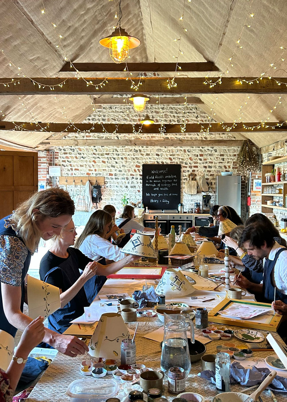 Grupa entuzjastów maluje wzory mandali na drewnianych deskach przy wspólnym stole z farbami