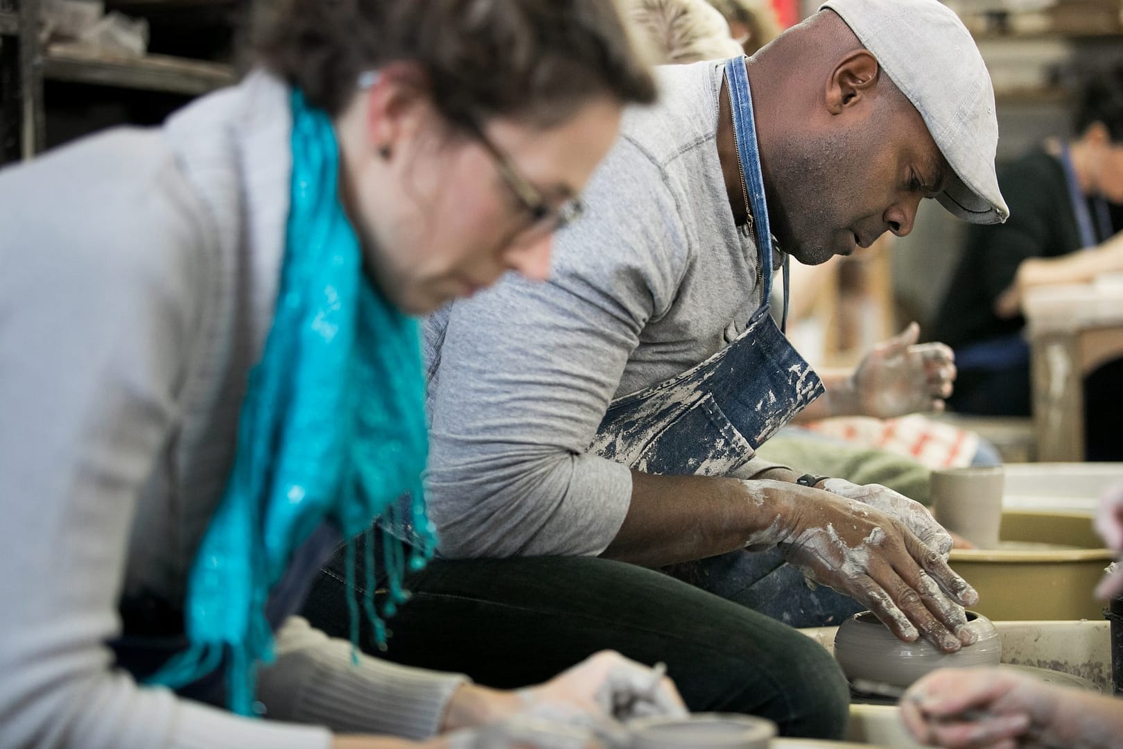 Uczestnicy dekorują ceramiczne misy pędzlami z angobami i szkliwami